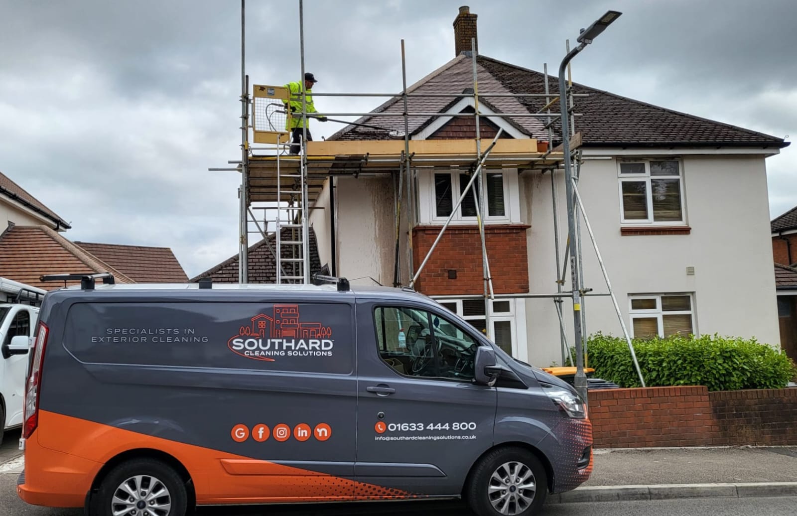 Southard Cleaning Solutions van and technician soft washing a roof from scaffolding